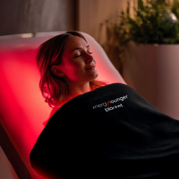 Person lying in a red light therapy chamber with 'energy harvest' branding.