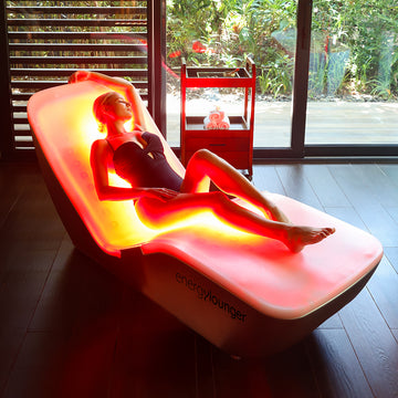 Person lying on a red energy lounge with 'energyYounger' branding in a room with large windows.