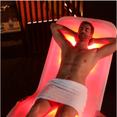 Person relaxing on a glowing red light therapy lounger in a dim wellness room.