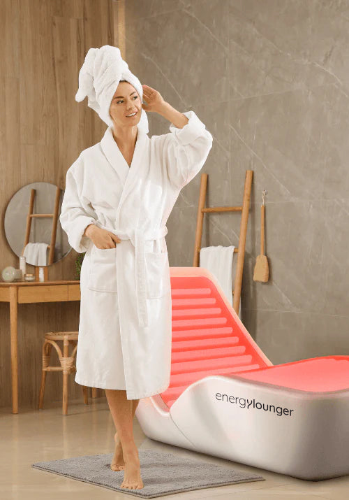 Woman standing in a spa wearing a bathrobe beside an Energylounger relaxation chair.